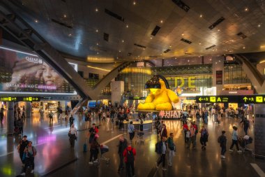 Doha, Katar, 27 Sep 2024 Çeşitli gezginlerle dolu canlı bir Hamad havaalanı terminali etkileyici modern mimari ve canlı atmosfer içeren çarpıcı bir altın heykele sahiptir.