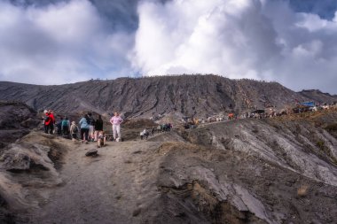 Java, Indonesia, 2 Oct 2024 A group of hikers explores a breathtaking Bromo volcanic landscape with dramatic clouds and rugged terrain, perfect for adventure seekers and nature lovers