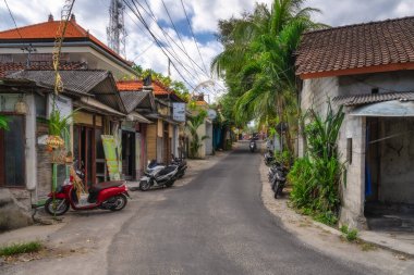 Nusa Lembongan, Bali, Endonezya, 06.10.25 Geleneksel evlerin, yemyeşil otlakların ve park edilmiş motosikletlerin yer aldığı pitoresk dar bir cadde