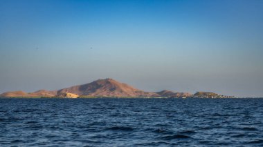 Bu güzel manzara, endonezya, Komodo takımadaları altında engebeli bir dağ silueti ve kıyıya vuran hafif dalgaları gösteren uzak bir adayı alacakaranlıkta yakalıyor.
