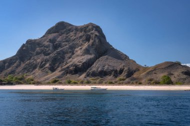 Nefes kesici güzellikte bu manzara, berrak mavi sular ve berrak gökyüzü, Padar Adası, Pink Beach, Komodo, Endonezya, Endonezya ile çevrili sakin bir plajın üzerinde zarifçe yükselen görkemli bir dağı gözler önüne seriyor.