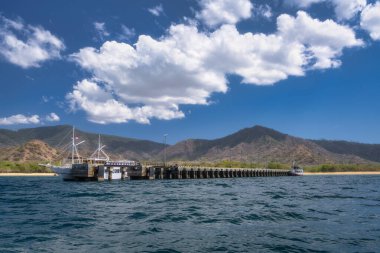 Muhteşem dağlara ve tüylü beyaz bulutlara, Komodo, Endonezya 'ya mükemmel bir şekilde ayarlanmış, küçük, çekici bir turist teknesinin güvenli bir şekilde kenetlendiği nefes kesici bir sahil manzarası.