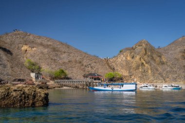 Komodo, Endonezya, 8 Ekim 2025 Padar Adası 'nın kayalık kıyılarına demirlemiş çok sayıda teknenin parlak mavi gökyüzü altında kurak ve kuru dağlarla çevrili olduğu çarpıcı ve pitoresk bir kıyı sahnesi.