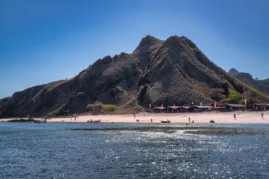 Komodo, Endonezya, 8 Ekim 2025 Padar Adası 'nda güzel bir pembe kumsal, engebeli bir dağın sahneyi sergiliyor, kıyıda hafif dalgalar dalgalanarak sakin bir atmosfer yaratıyor.