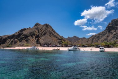 Komodo, Endonezya, 8 Ekim 2025 Turkuaz suları, altın kumu, sallanan tekneleri ve yukarıdaki görkemli dağlarıyla Padar Adası 'nın büyüleyici pembe plajı doğada dinlenmek için mükemmel bir tropikal kaçış.