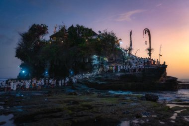 Bali, Endonezya, 10 Ekim 2024 Günbatımında Tanah Lot Tapınağı 'nın büyüleyici ve büyüleyici manzarası, ziyaretçilerin nefes kesici kayalık kıyı şeridi boyunca Pujawali Töreni' nin keyfini çıkardıkları görülebilir.