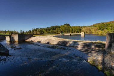 Huzurlu ve huzurlu bir su yolu, büyüleyici kırsal yapılar ve canlı yeşillikler barındırıyor, hepsi açık ve parlak mavi gökyüzü altında, Bohernabreena Reservoir, Dublin, İrlanda