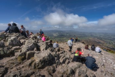 Wicklow, İrlanda, 25 Nisan 2021. Bir grup hevesli yürüyüşçü Sugar Loaf dağının kayalık zirvesinde güzel manzaranın nefes kesici ve nefes kesici manzarasının tadını çıkarıyorlar.