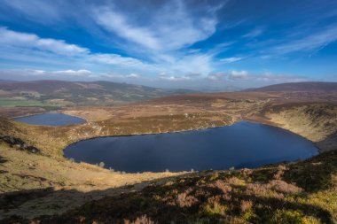 Yuvarlanan tepelerin arasına yerleşmiş sakin Bray göllerinin nefes kesici manzarasının tadını çıkarın. Hepsi de doğanın inanılmaz görkemini gözler önüne seren parlak mavi gökyüzüne karşı kurulmuş. Wicklow, İrlanda.