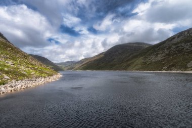 Huzurlu bir dağ gölü, Ben Crom Rezervuarı, Yas Dağları 'nın yuvarlanan yeşil tepeleri arasında güzel bir yer, dramatik bulutlu bir gökyüzü altında yakalandı, doğa severleri için ideal, Kuzey İrlanda
