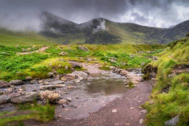 Bereketli, canlı yeşillik ve dramatik bulutlar gökyüzünde yuvarlanan İrlanda, Kerry, Kerry 'nin yer aldığı sakin ve sakin bir dağ manzarası gözler önüne seriliyor.