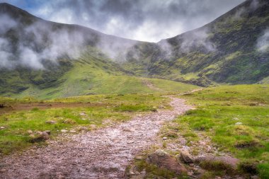Bereketli yeşil Carrauntoohil dağının sakin manzarası ve puslu mesafeye dolambaçlı bir yol. Güzellik ve macera peşinde koşan doğa aşıkları için ideal, Kerry, İrlanda