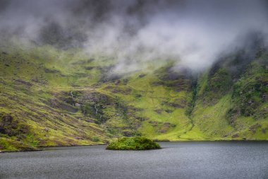 Huzurlu ve sakin bir dağ gölü güzel bir şekilde yemyeşil tepelerle çevrelenmiş ve yumuşak sisle kaplanmış, huzurlu ve huzurlu bir doğal manzara yaratıyor, Kerry, İrlanda