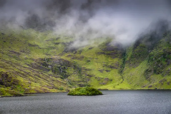 Huzurlu ve sakin bir dağ gölü güzel bir şekilde yemyeşil tepelerle çevrelenmiş ve yumuşak sisle kaplanmış, huzurlu ve huzurlu bir doğal manzara yaratıyor, Kerry, İrlanda