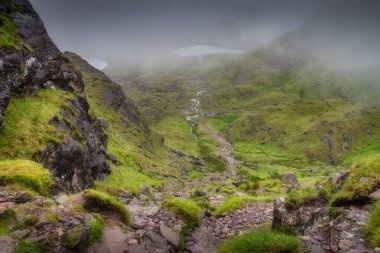 Sarp Carrauntoohil dağı tarafından güzel çerçevelenmiş, nefes kesici bir vadi manzarası ve hafif kıvrımlı bir akarsu, doğada bol miktarda canlı yeşil çimenler sergiliyor, Kerry, İrlanda