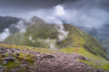 Yumuşak bir sisle kaplanmış yemyeşil dağlık arazinin nefes kesici bir görüntüsü, dinamik, bulutlu bir gökyüzü altında, mükemmel bir şekilde yansıtan doğanın özü, Kerry, İrlanda