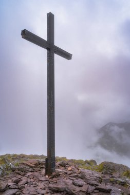 Carrauntoohil dağının tepesinde görkemli bir haç duruyor, kalın bir sis ile örtülmüş, nefes kesen bir dağ zeminine karşı inanç ve sükuneti temsil ediyor, Kerry, İrlanda