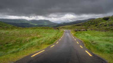 Dolambaçlı bir yol renkli tarlalarda ve nazik tepelerde dolanıyor, doğa aşıklarını büyüleyici bir gökyüzü altında bu büyüleyici manzarayı keşfetmeye davet ediyor, Kerry, İrlanda