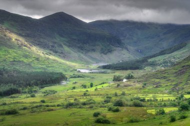 Yuvarlanan dağların arasına yerleştirilmiş gür, canlı bir Kara Vadi 'nin huzurlu ve resimsel manzarası karamsar, bulutlu gökyüzünün altında gerçekten sakin bir manzara sergiliyor, Kerry, İrlanda