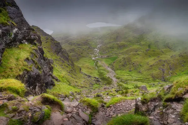 Sarp Carrauntoohil dağı tarafından güzel çerçevelenmiş, nefes kesici bir vadi manzarası ve hafif kıvrımlı bir akarsu, doğada bol miktarda canlı yeşil çimenler sergiliyor, Kerry, İrlanda