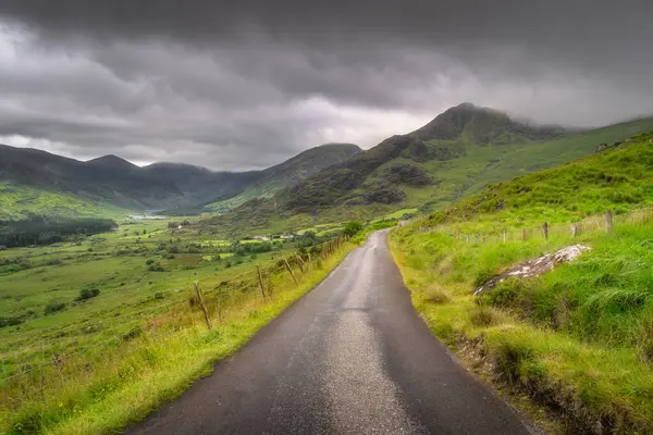 Kara Vadi 'nin canlı, renkli tepelerinde zarif rüzgarlar estiren sakin kırsal bir yol keşfedin. Görkemli bulutlar çarpıcı manzaranın nefes kesici manzarasını cesaretlendirsin, Kerry, İrlanda.