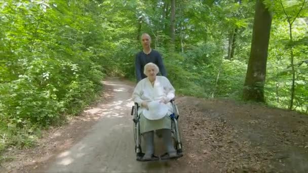 Mann Fährt Mit Alter Frau Rollstuhl Waldspaziergang — Stockvideo