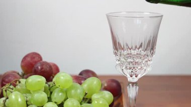 Kırmızı şarap bardağa doluyor. Arkaplanda üzümler.