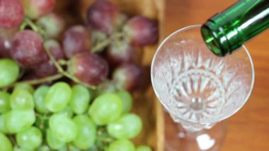 Kırmızı şarap bardağa doluyor. Arkaplanda üzümler.