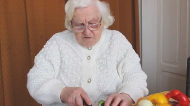 Yaşlı bir kadın yeşil biber dilimliyor ve vejetaryen yemeği hazırlıyor. 
