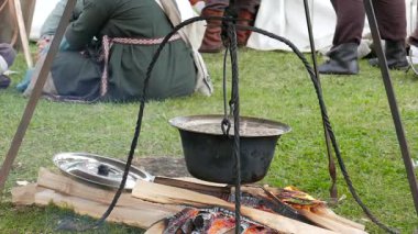 Çorba demir bir tencerede pişer. Arka planda ortaçağ kıyafeti insanlar