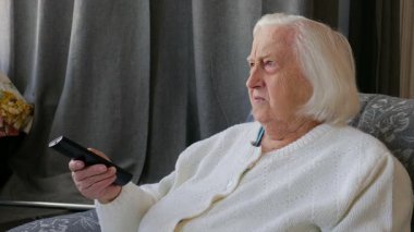 Yaşlı, kıdemli kadın bir koltukta oturuyor ve evde televizyon izliyor.. 