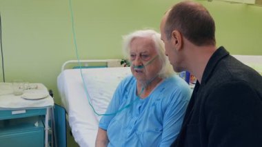 Yaşlı, hasta kadın ve onun aile üyesi hastane odasında konuşuyor