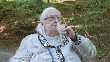 Tekerlekli sandalyedeki yaşlı kadın su ya da alkol içiyor.