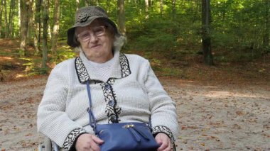 Tekerlekli sandalyedeki yaşlı kadın gülümsüyor. Orman arka planda