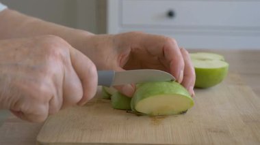 Kadın kıdemli yeşil elma kesiyor. Closeup elinde