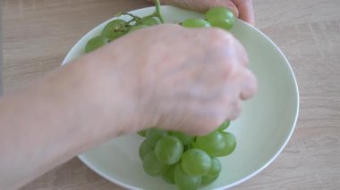 Yaşlı kadın üzüm yiyor. Bir tabak ve ellerle yakınlaş.