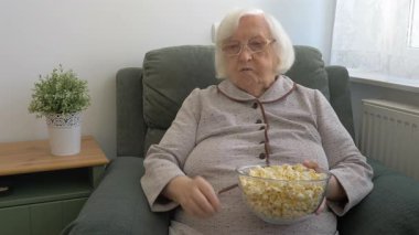 Yaşlı kadın patlamış mısır yiyor ve televizyon izliyor..