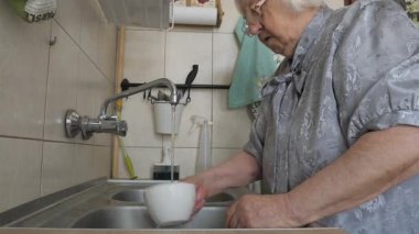 Yaşlı kadın bulaşık yıkıyor.