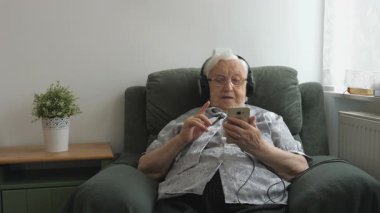 Yaşlı kadın bir akıllı telefonda müzik (eski hit) dinliyor.