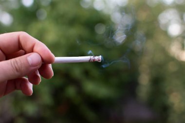 Doğanın arka planında sigara içerek sigara yakmak. Yüksek kalite fotoğraf