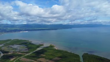 Deniz kıyısı manzarası, dağlar, deniz ve bulutlar mavi gökyüzünde. 