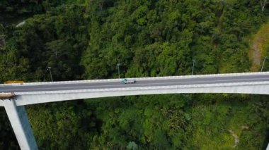 Arabalar uçurumun üzerindeki yüksek bir köprü boyunca yol alırlar. Tropikal dağlar arasındaki yüksek köprü. Agas Agas Köprüsü.