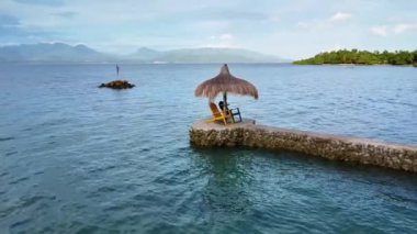 Denizde palmiye yapraklarından yapılmış çatısı olan tropikal manzaralı teras.