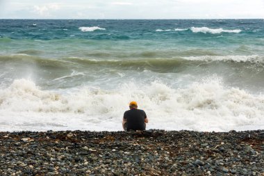 Yalnız bunalımlı insan okyanus kıyısında öfkeli dalgalarla tek başına oturuyor..