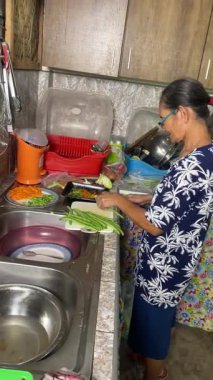 Yaşlı bir Asyalı kadın ev mutfağında sebzelerden yemek hazırlıyor..