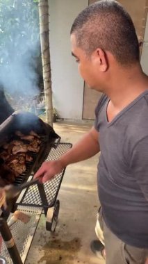 Adam et ızgarasına et koyuyor geleneksel şekilde et pişirmek için ateş, kömür ve barbekü pişiriyor..