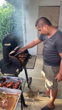 Adam ızgaradan pişmiş eti alıp tepsiye koyuyor, barbekü hazırlıyor..