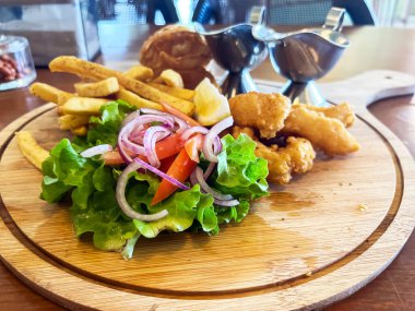 Tahta tepside balık ve patates kızartması, soslar ve kafedeki bir masada taze sebzeler.. 