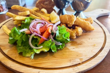 Tahta tepside balık ve patates kızartması, soslar ve kafedeki bir masada taze sebzeler.. 