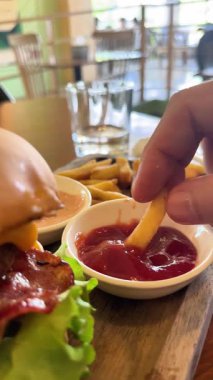 Hamburgerin önünde patates kızartmasını ketçapa batırmak, fast food.